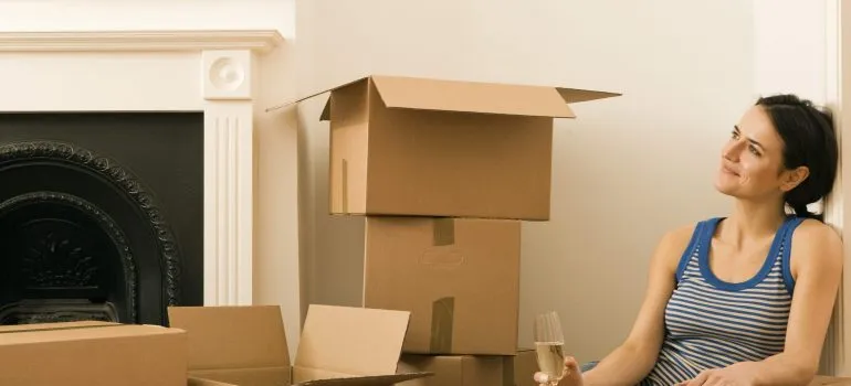 a girl sitting next to a pile of moving boxes waiting for movers Star ID to help her move
