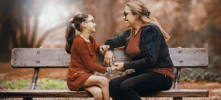 A mother and daughter sitting on a bench and talking.
