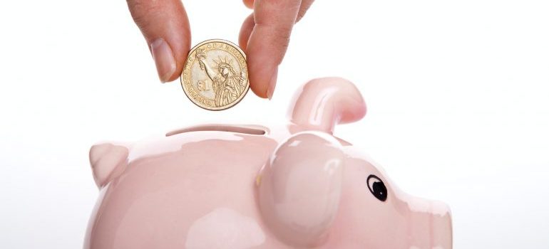 person placing a coin in piggy bank before choosing between storage containers vs storage units