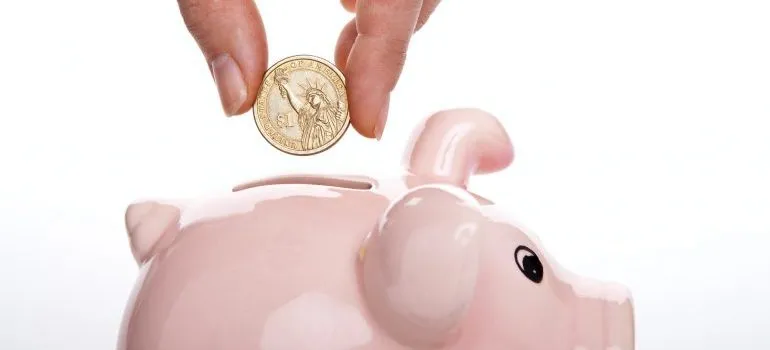 person placing a coin in piggy bank before choosing between storage containers vs storage units