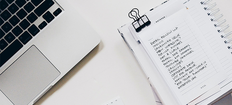 A to-do list next to a laptop on a white desk