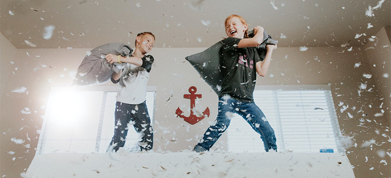 Two kids pillow fighting on a bed