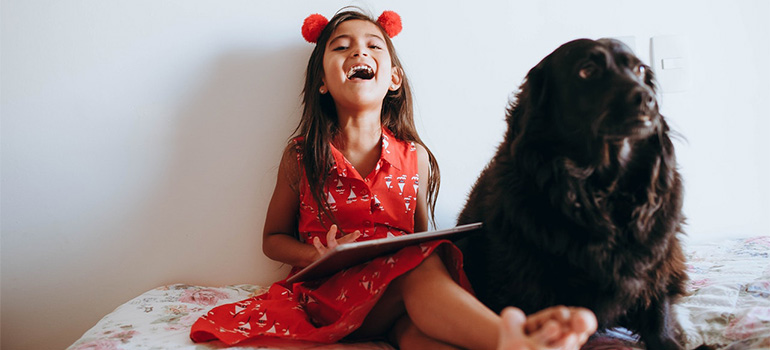 A girl sitting on a bed with a black dog, smiling and holding abook