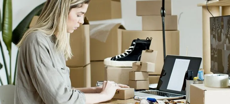 A woman working on a laptop next to boxes.