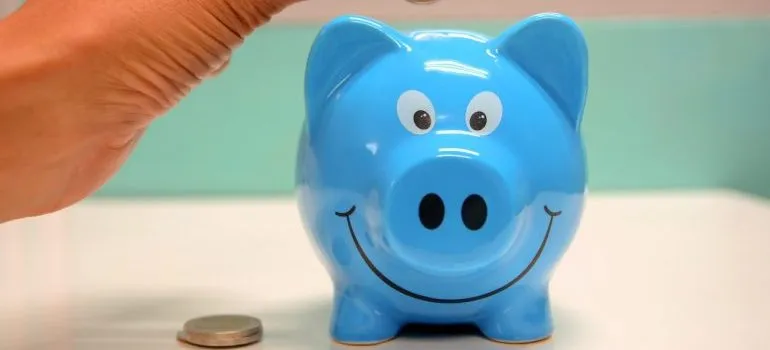 A person putting a coin in a blue piggy bank.