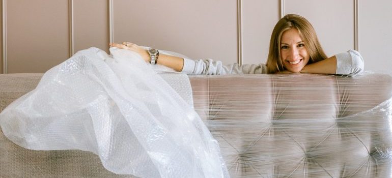 A smiling woman leaning on a wrapped sofa.