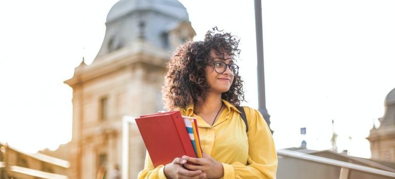 A student in yellow jacket holding notebooks.