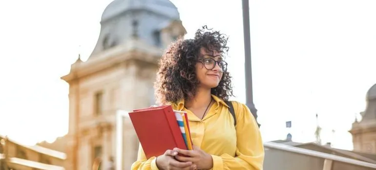A student in yellow jacket holding notebooks.