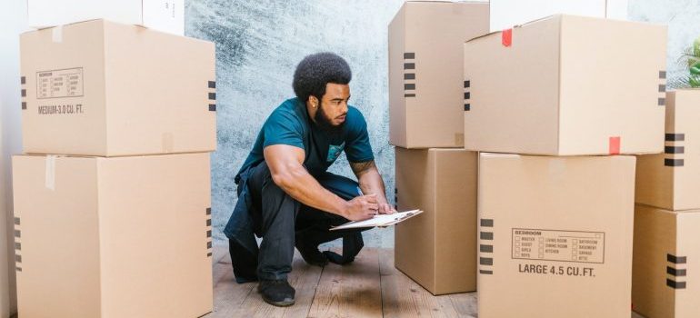 A man among moving boxes writing in a notepad