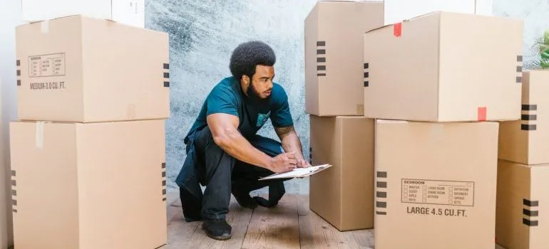 A man among moving boxes writing in a notepad