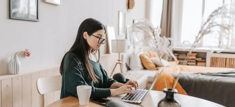 A woman with glasses using laptop to find out how to make moving as a student easier.