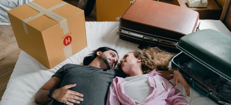 A young couple laying on the bed next to suitcases.