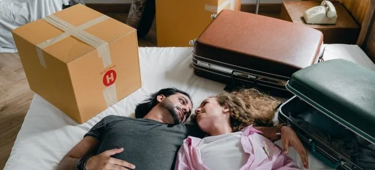 A young couple lying on a bed among suitcases.