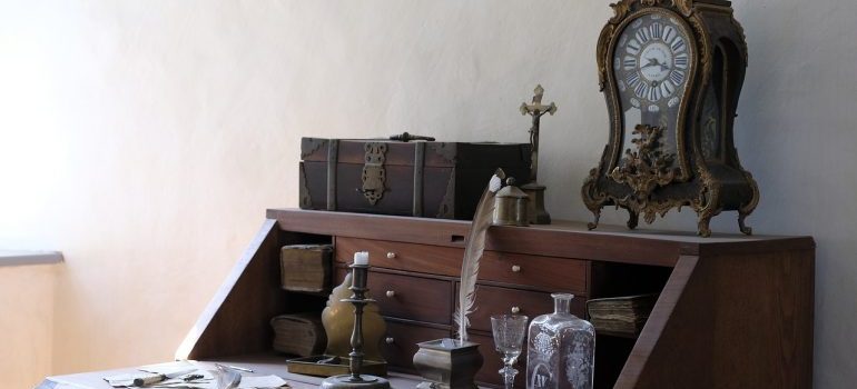 A small grandfather clock on an antique desk.