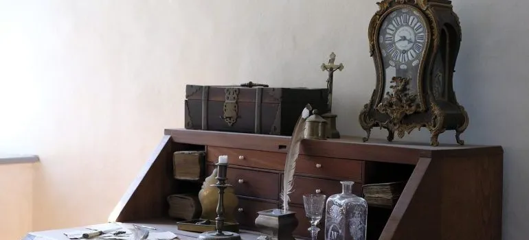 A small grandfather clock on an antique desk.