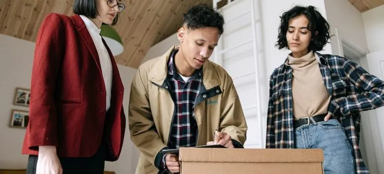 A man between two women signing papers on a moving box