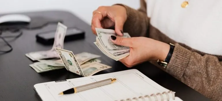 A person sitting at a table with a stack of banknotes and a planner 