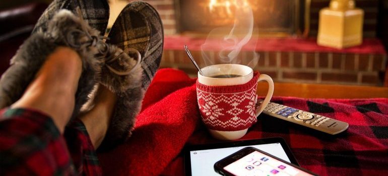 A person in front of a fireplace with a cup of coffee and a phone.