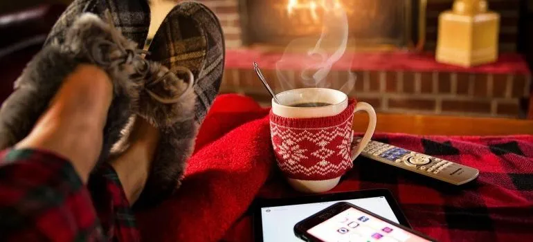 A person in front of a fireplace with a cup of coffee and a phone.