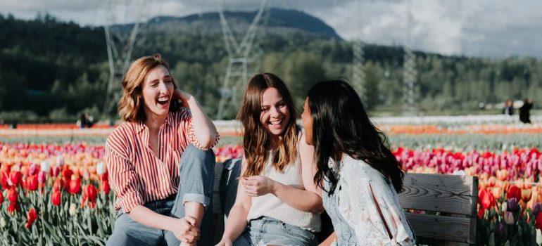 three women sitting on a bench, laughing