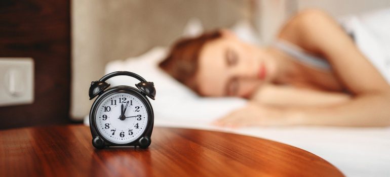 A woman sleeping next to an alarm clock.
