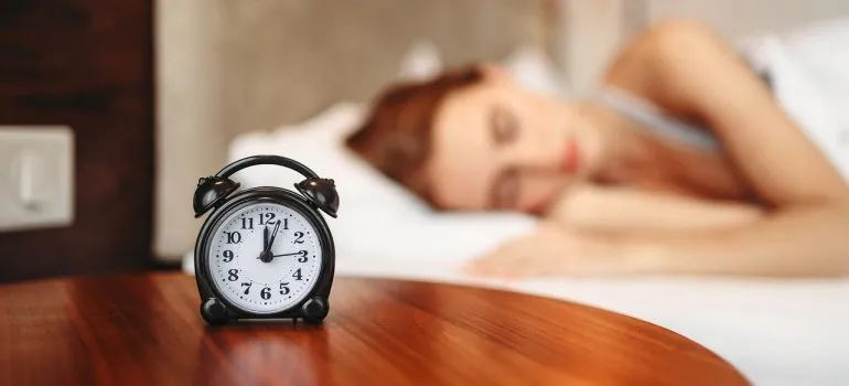 A woman sleeping next to an alarm clock.