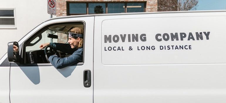 A man driving a white moving van pondering pros and cons of choosing a moving company based on prices.