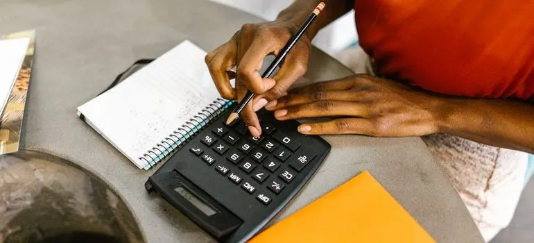 A woman's hands typing on a calculator with a notepad and a file on the side.