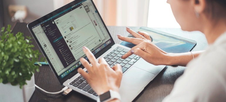 A woman is sitting and reading some data from the laptop screen, checking signs of a successful relocation.