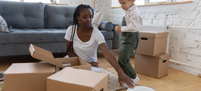 a woman on the floor with a child putting plates in a box