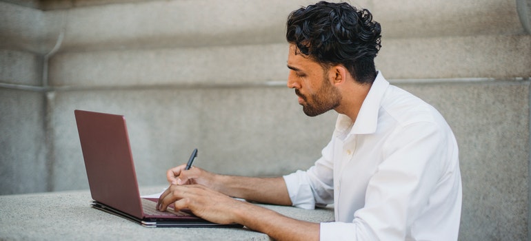 a man writing something in front of a laptop