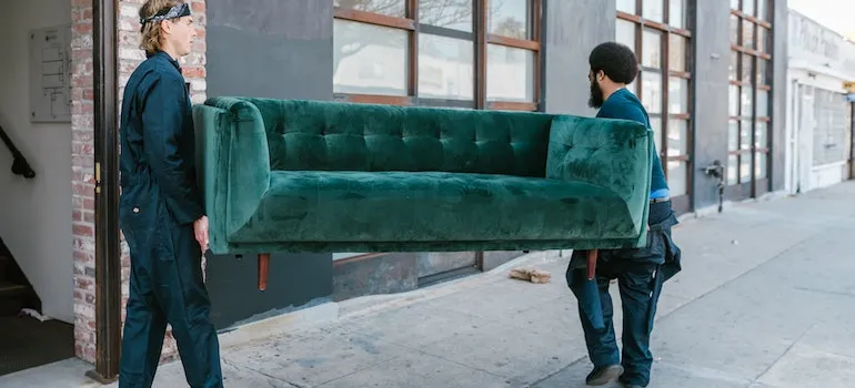 Two movers carrying a green sofa