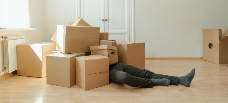 a man under the boxes is burdened by the choice of cardboard vs plastic moving boxes