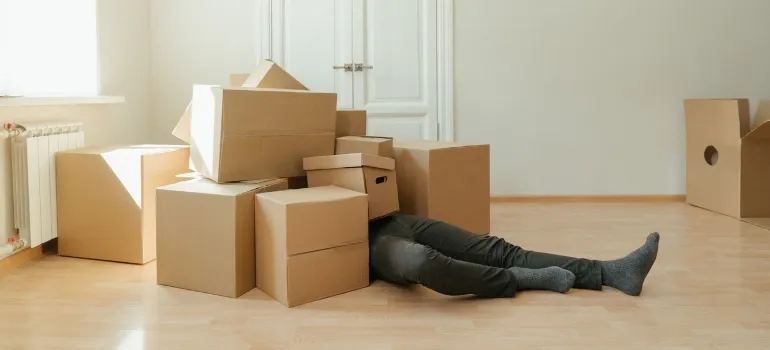 a man under the boxes is burdened by the choice of cardboard vs plastic moving boxes