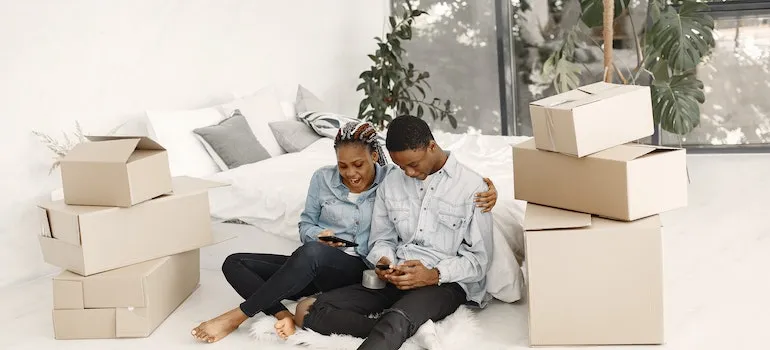 A couple sitting on the floor among moving boxes searching for things to remember when planning a move on their smartphones