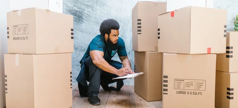 A Bearded Man Crouching Looking at Cardboard Boxes