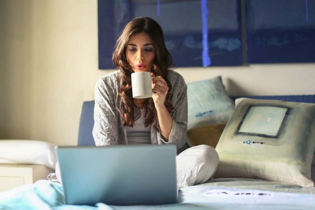 Woman sitting on bed with laptop, holding a mug