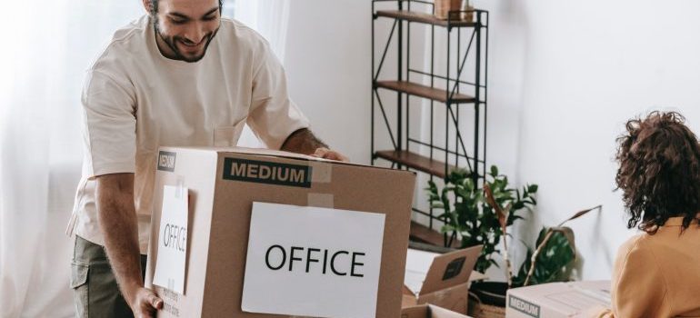 A man carrying a box labeled OFFICE to mobile storage for commercial purposes
