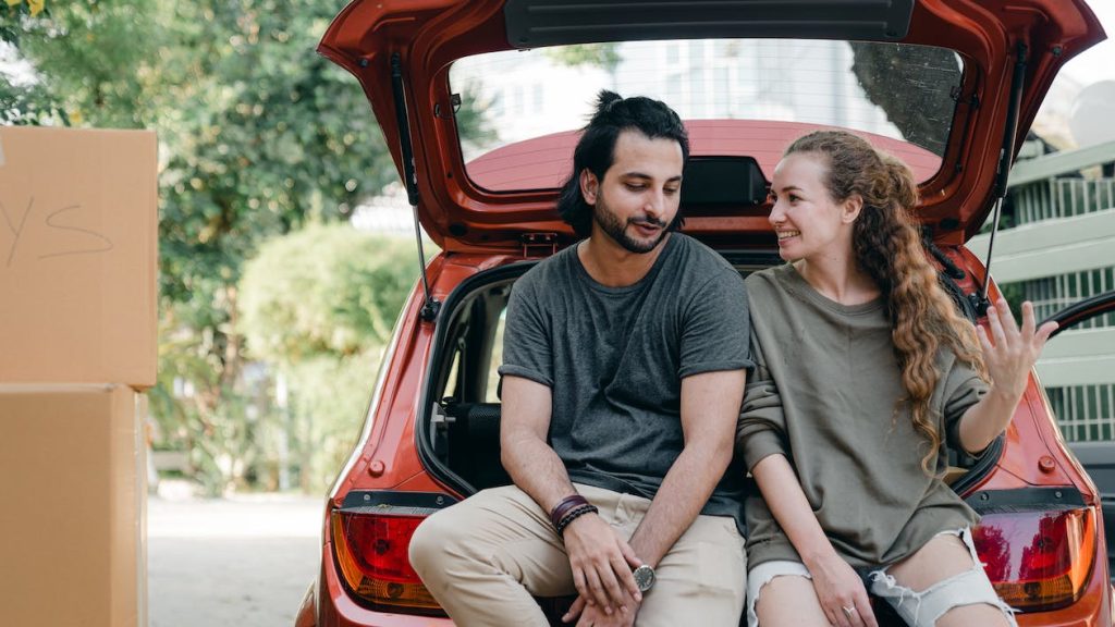 A couple sitting on the back of their car after moving