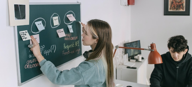 A woman exploring ways for timely equipment shipments for medical start-ups written on a green board