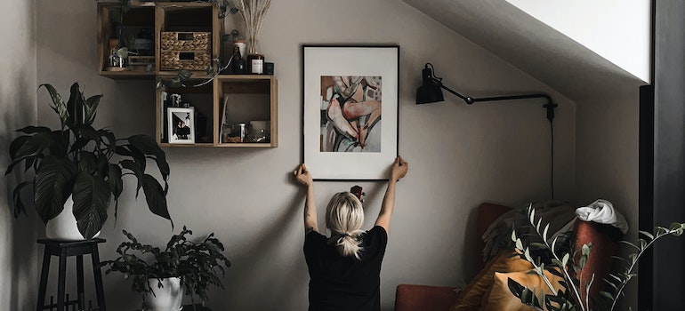 A woman hanging a painting in a bedroom while personalizing your Boise home