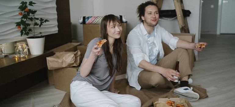 A couple sitting on the floor eating pizza after using digital tools for budget-friendly Idaho moves