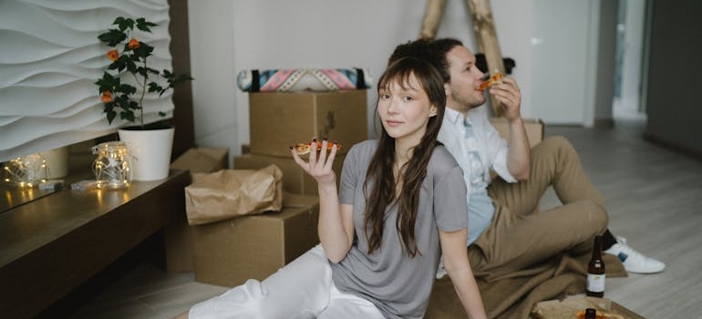 A Couple Eating Pizza while Sitting on the Floor among moving boxes
