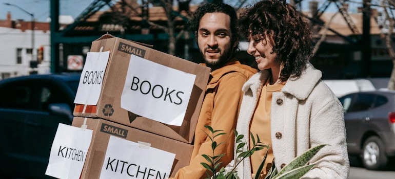 Man Carrying Boxes And Woman Holding A Box Of Plants