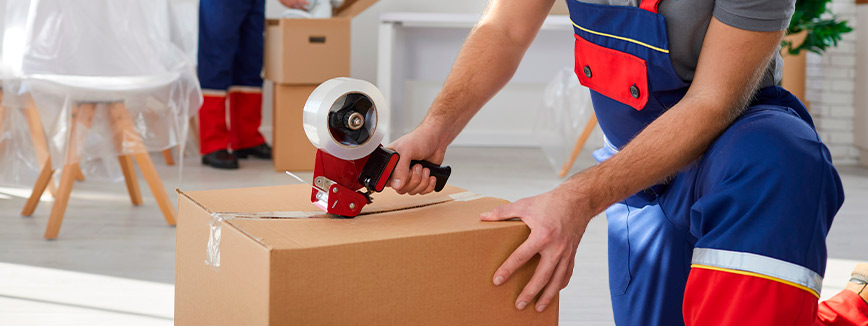 A man in overalls uses a box cutter to slice through cardboard while preparing for a local move in Boise, Idaho.