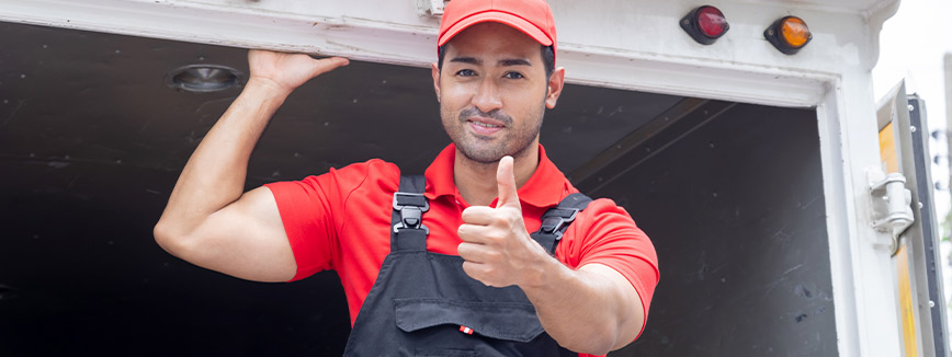 A man in a red shirt and overalls gives a thumbs up, representing Peasley Movers in Boise, Idaho.