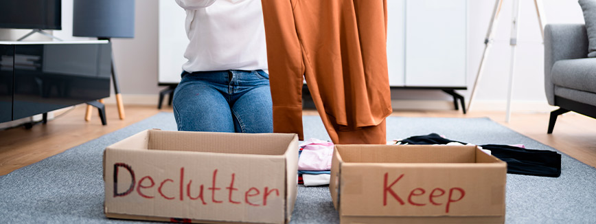 A woman on the floor with boxes and a declutter sign, organizing her belongings for a move from Idaho to California.