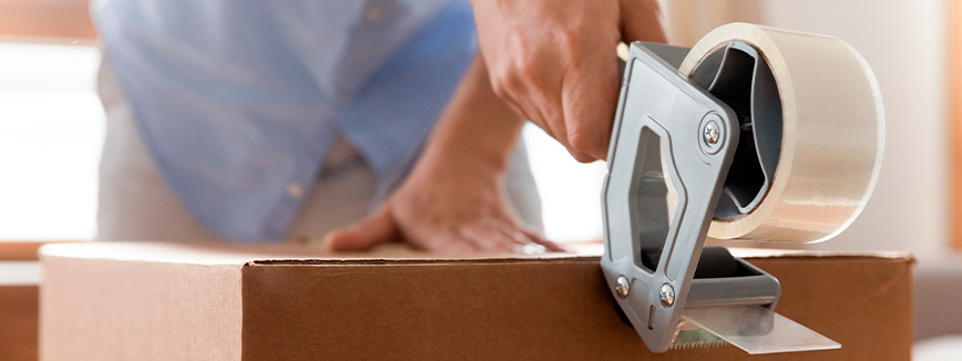 A person securing a box with tape, illustrating cost-saving strategies for moving from Idaho to Texas.