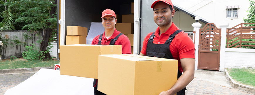 Two men in red shirts and black pants carry boxes while moving from Idaho to Colorado during the fall season.