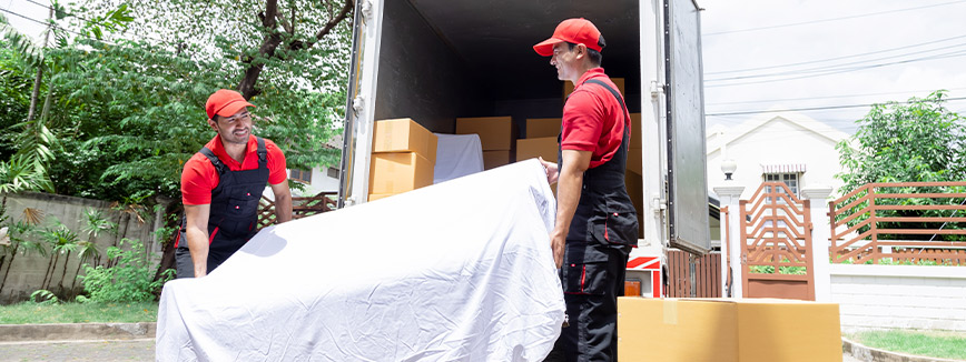 Two men in red shirts lift a large white sheet, demonstrating the efficiency of professional movers in Meridian.